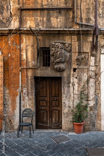 Photography Jewish quarter, in the ghetto, detail of a wooden door of an orange building, with inserts of ancient Roman inscriptions, bas-relief of a lion, a chair and a plant, Lungotevere, Rome