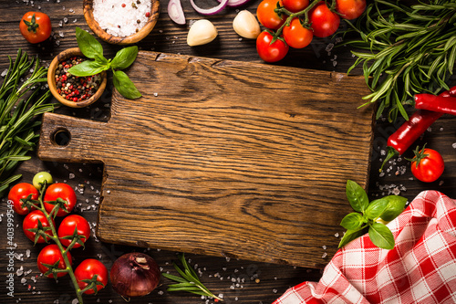 Food cooking background with cutting board, spices, herbs and vegetables at wooden kitchen table. Top view with copy space.