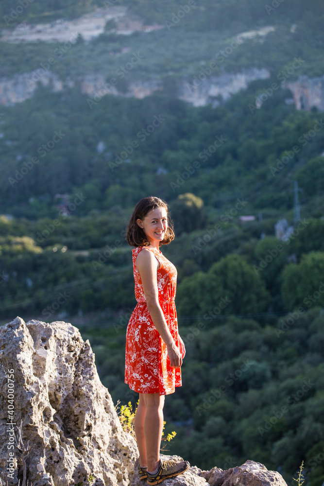 A girl in a red dress on a large rock on top of a mountain