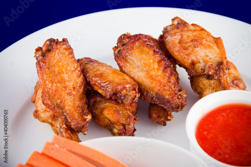 Roasted chicken wings and dipping sauce on white plate on blue background