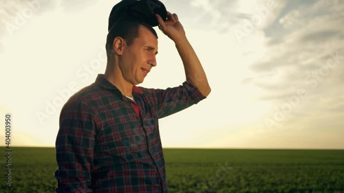 Farmer agronomist in the field at sunset. Ecoculture farm. Senior farmer, business owner looks at the camera in the field. Senior agronomist adjusts his cap and hat. Farmer agronomist checks eco-crops photo