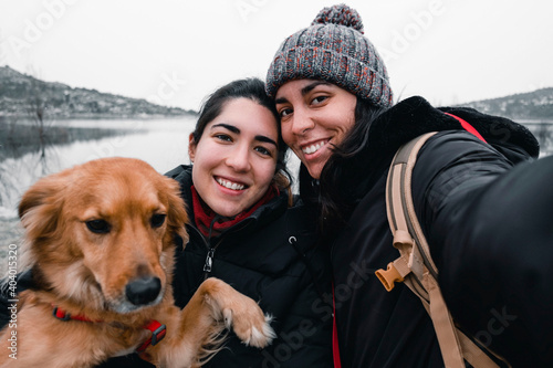 Self-portrait of 2 young girls with a dog in winter clothes. Family concept. LGTB concept. Friendship