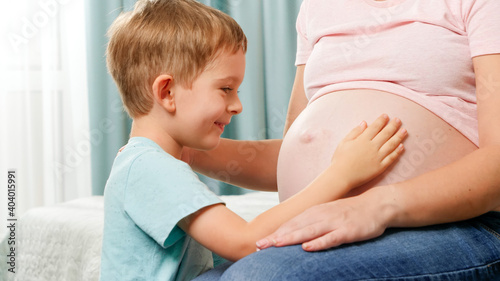 Happy smiling toddler boy touching big belly of his pregnant mother waiting for baby