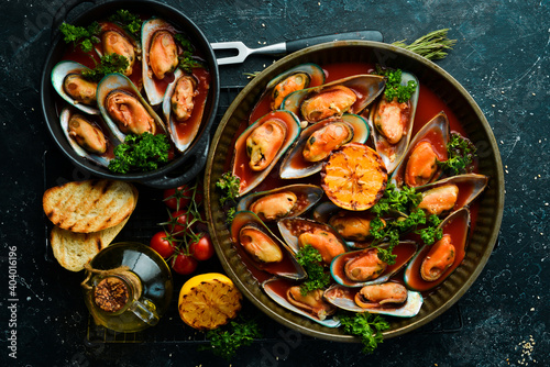 Cooked mussels with tomato sauce, garlic, parsley and lemon. Seafood. Free space for text. On a stone background.