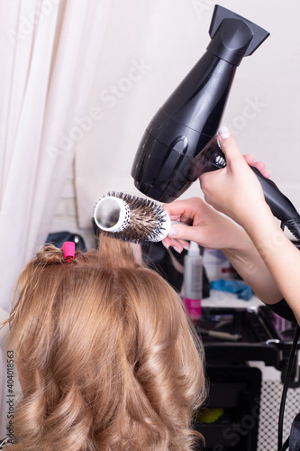 Female hairdresser's hands brushing and blow drying blonde hair in beauty salon
