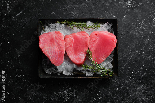 Raw tuna steak with spices on ice. On a dark background. Top view.