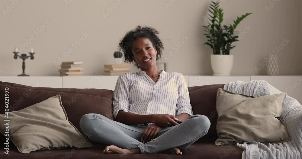 In cozy living room African woman enjoy free time relaxing on comfy sofa holding remote control, switch channels, watch tv series show, spend weekend at home. Streaming digital television ad concept In cozy living room African woman enjoy free time relaxing on comfy sofa holding remote control, switch channels, watch tv series show, spend weekend at home. Streaming digital television ad concept