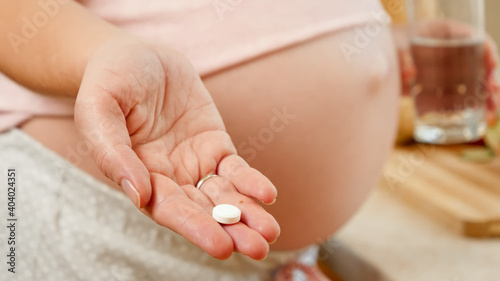 Closeup of young woman expecting baby holding medical pill or vitamin on hand. Concept of healthy lifestyle, nutrition and hydration during pregnancy