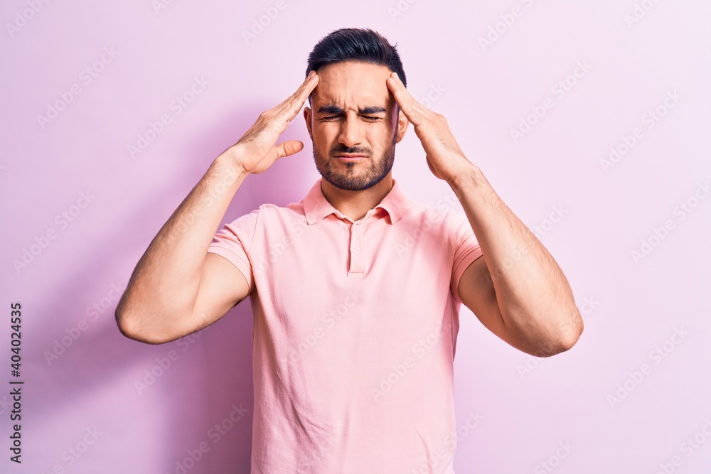 Young handsome man with beard wearing casual polo standing over pink background with hand on head, headache because stress. Suffering migraine. Young handsome man with beard wearing casual polo standing over pink background with hand on head, headache because stress. Suffering migraine.