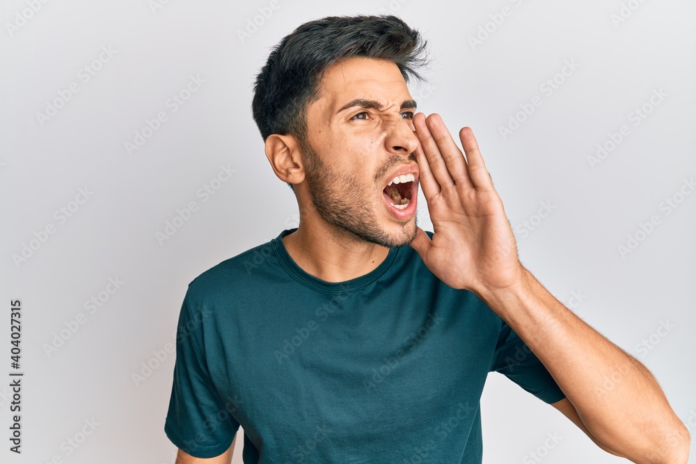 Young handsome man wearing casual clothes shouting and screaming loud to side with hand on mouth. communication concept. Young handsome man wearing casual clothes shouting and screaming loud to side with hand on mouth. communication concept.