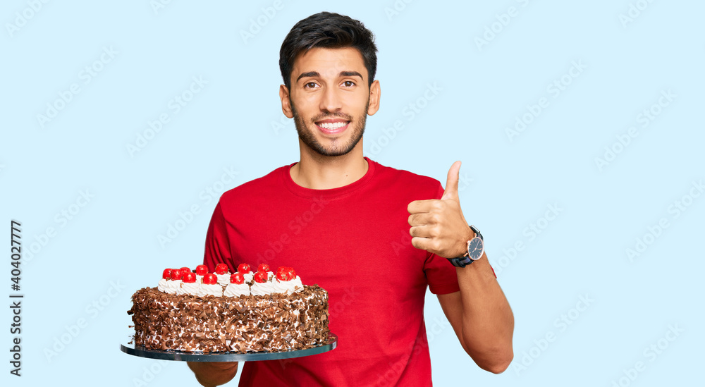 Young handsome man celebrating birthday with cake smiling happy and positive, thumb up doing excellent and approval sign Young handsome man celebrating birthday with cake smiling happy and positive, thumb up doing excellent and approval sign