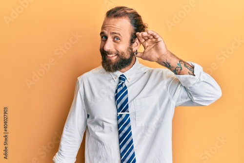 Handsome man with beard and long hair wearing business clothes smiling with hand over ear listening an hearing to rumor or gossip. deafness concept.