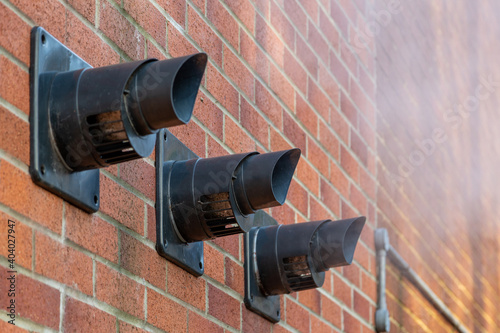 Three central heating boiler flues releasing steam on the exterior of a brick house