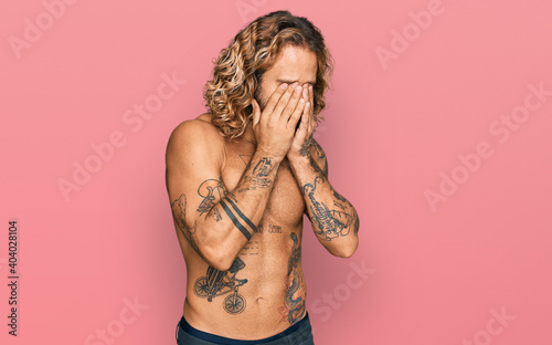 Fotografia Handsome man with beard and long hair standing shirtless showing tattoos rubbing eyes for fatigue and headache, sleepy and tired expression