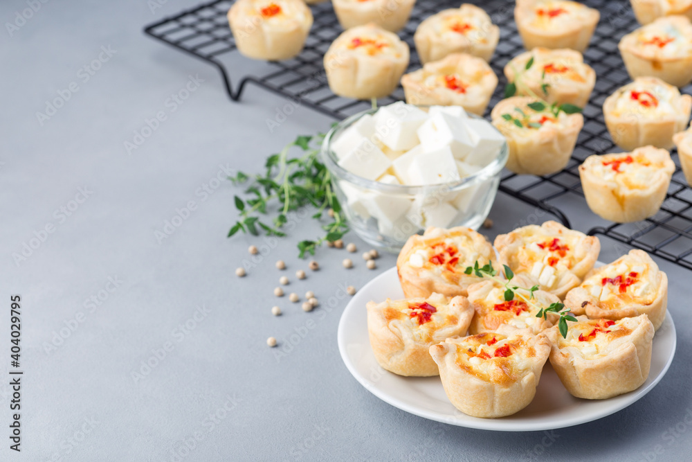 Mini quiche muffins with feta cheese, fried onion, thyme and red bell pepper, on white plate and cooling rack, horizontal, copy space