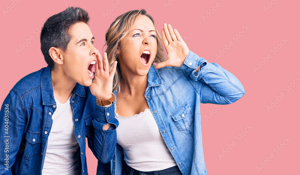 Couple of women wearing casual clothes shouting and screaming loud to side with hand on mouth. communication concept. Couple of women wearing casual clothes shouting and screaming loud to side with hand on mouth. communication concept.