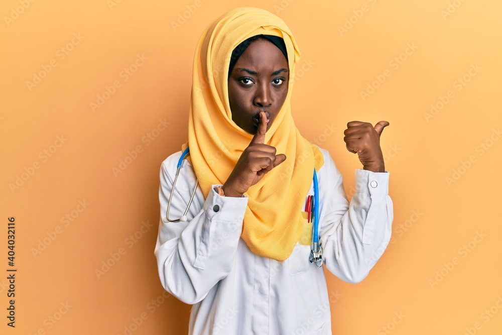 Beautiful african young woman wearing doctor uniform and hijab asking to be quiet with finger on lips pointing with hand to the side. silence and secret concept.