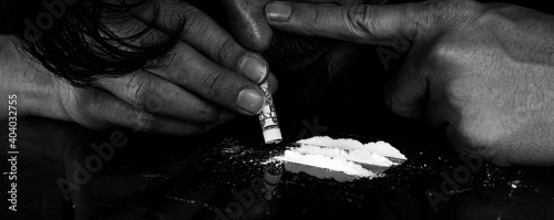 Drug addict man snorting cocaine powder with rolled dollar banknote. Narcotics concept. Dramatic monochrome, black and white photo. Close-up macro shot. Panoramic shot. Panorama banner.