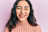 Hispanic teenager girl with dental braces showing orthodontic brackets looking positive and happy standing and smiling with a confident smile showing teeth