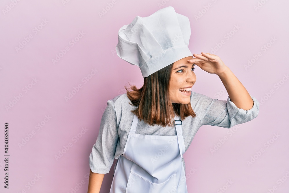 Young beautiful woman wearing professional cook uniform and hat very happy and smiling looking far away with hand over head. searching concept. Young beautiful woman wearing professional cook uniform and hat very happy and smiling looking far away with hand over head. searching concept.