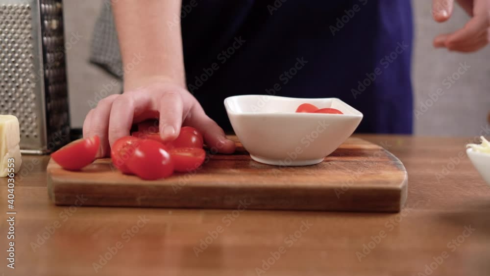 the chef takes the sliced slices of red and ripe cherry tomatoes with his hands, puts them on a plate. Pizza ingredients concept the chef takes the sliced slices of red and ripe cherry tomatoes with his hands, puts them on a plate. Pizza ingredients concept