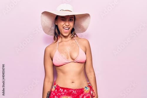 Young woman wearing bikini and hat winking looking at the camera with sexy expression, cheerful and happy face.