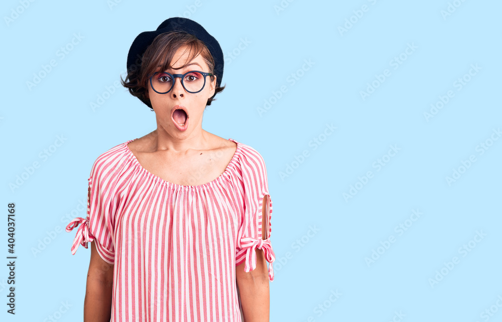 Beautiful young woman with short hair wearing casual clothes and glasses scared and amazed with open mouth for surprise, disbelief face Beautiful young woman with short hair wearing casual clothes and glasses scared and amazed with open mouth for surprise, disbelief face