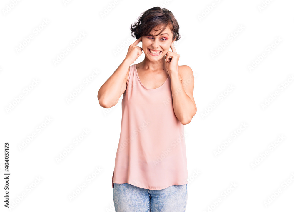 Beautiful young woman with short hair wearing casual style with sleeveless shirt covering ears with fingers with annoyed expression for the noise of loud music. deaf concept. Beautiful young woman with short hair wearing casual style with sleeveless shirt covering ears with fingers with annoyed expression for the noise of loud music. deaf concept.