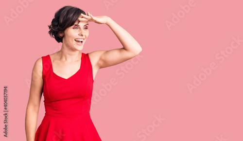 Beautiful young woman with short hair wearing casual style with sleeveless shirt very happy and smiling looking far away with hand over head. searching concept.