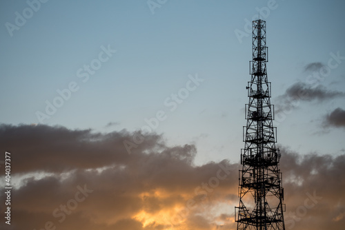 Cell phone relay tower. The construction of the mast against the blue sky and clouds illuminated by the yellow light of the setting sun.