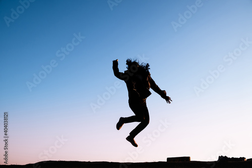Silhouette of woman jumping on blue sky background. The concept of happy people.