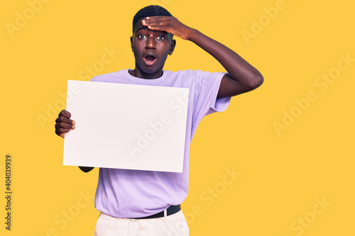 Young african american man holding blank empty banner stressed and frustrated with hand on head, surprised and angry face
