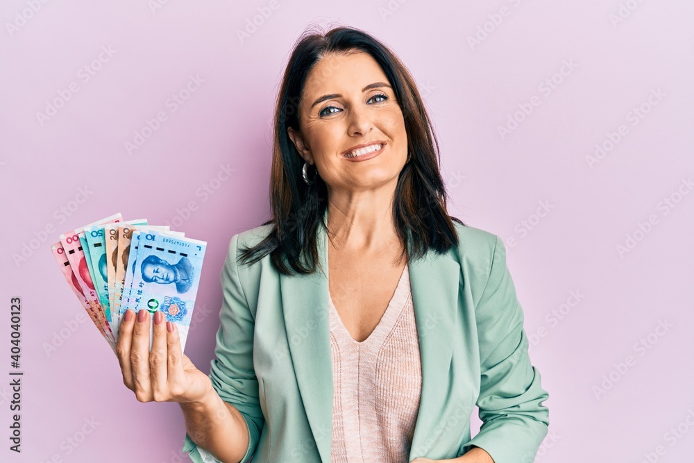 Middle age brunette woman holding yuan chinese banknotes looking positive and happy standing and smiling with a confident smile showing teeth Middle age brunette woman holding yuan chinese banknotes looking positive and happy standing and smiling with a confident smile showing teeth