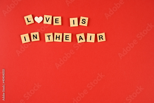  Valentine's Day background. wooden letters making the phrase love is in the air on a red background. Valentine's Day concept. Flat view, top view, copy space