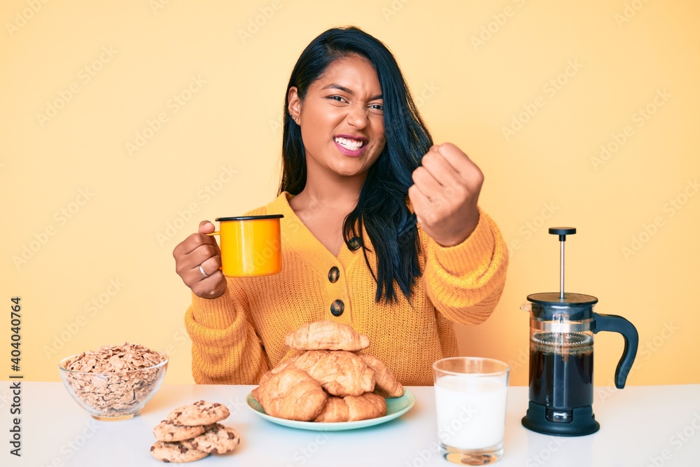 Beautiful latin young woman with long hair sitting on the table having breakfast annoyed and frustrated shouting with anger, yelling crazy with anger and hand raised Beautiful latin young woman with long hair sitting on the table having breakfast annoyed and frustrated shouting with anger, yelling crazy with anger and hand raised