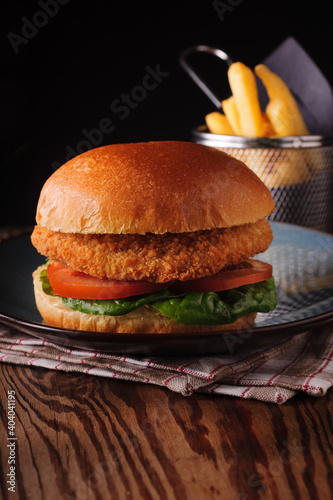 Chicken fillet in a in a brioche bun with lettuce tomatoes and fries shot with creative lighting