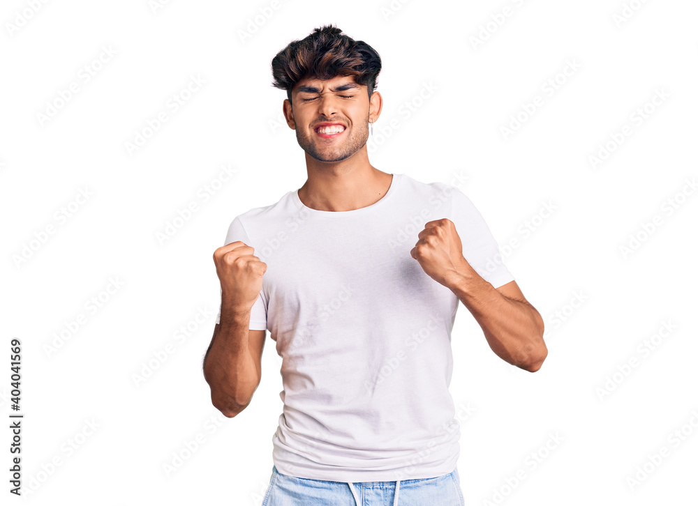 Young hispanic man wearing casual clothes very happy and excited doing winner gesture with arms raised, smiling and screaming for success. celebration concept. Young hispanic man wearing casual clothes very happy and excited doing winner gesture with arms raised, smiling and screaming for success. celebration concept.