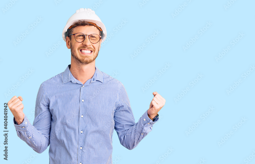 Handsome young man with bear wearing architect hardhat very happy and excited doing winner gesture with arms raised, smiling and screaming for success. celebration concept. Handsome young man with bear wearing architect hardhat very happy and excited doing winner gesture with arms raised, smiling and screaming for success. celebration concept.