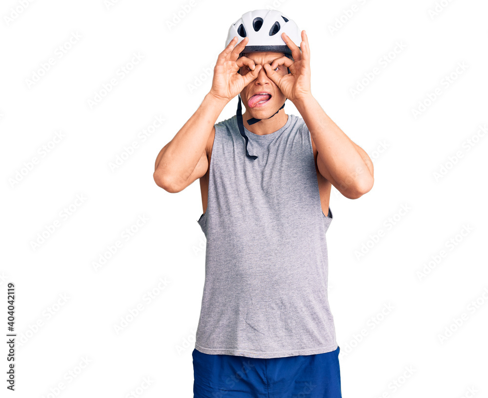 Fototapeta premium Young handsome man wearing bike helmet doing ok gesture like binoculars sticking tongue out, eyes looking through fingers. crazy expression.