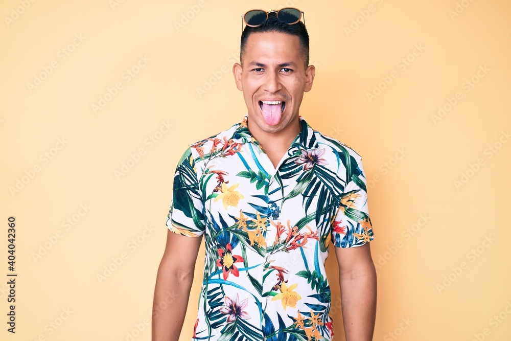 Young handsome latin man wearing summer clothes sticking tongue out happy with funny expression. emotion concept. Young handsome latin man wearing summer clothes sticking tongue out happy with funny expression. emotion concept.