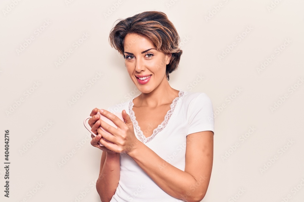 Young beautiful woman holding coffee looking positive and happy standing and smiling with a confident smile showing teeth Young beautiful woman holding coffee looking positive and happy standing and smiling with a confident smile showing teeth