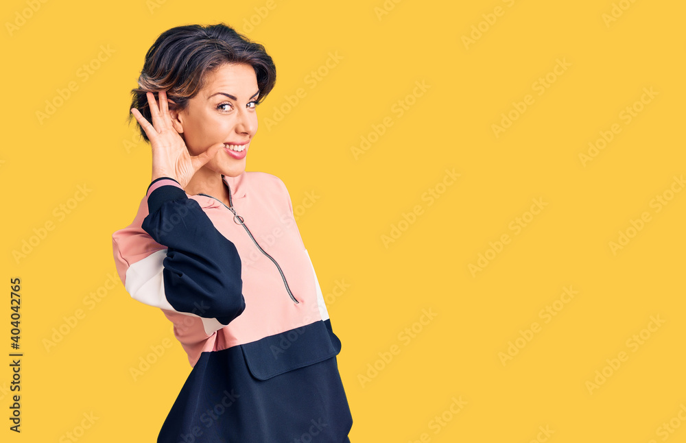 Young beautiful woman wearing sportswear smiling with hand over ear listening an hearing to rumor or gossip. deafness concept. Young beautiful woman wearing sportswear smiling with hand over ear listening an hearing to rumor or gossip. deafness concept.