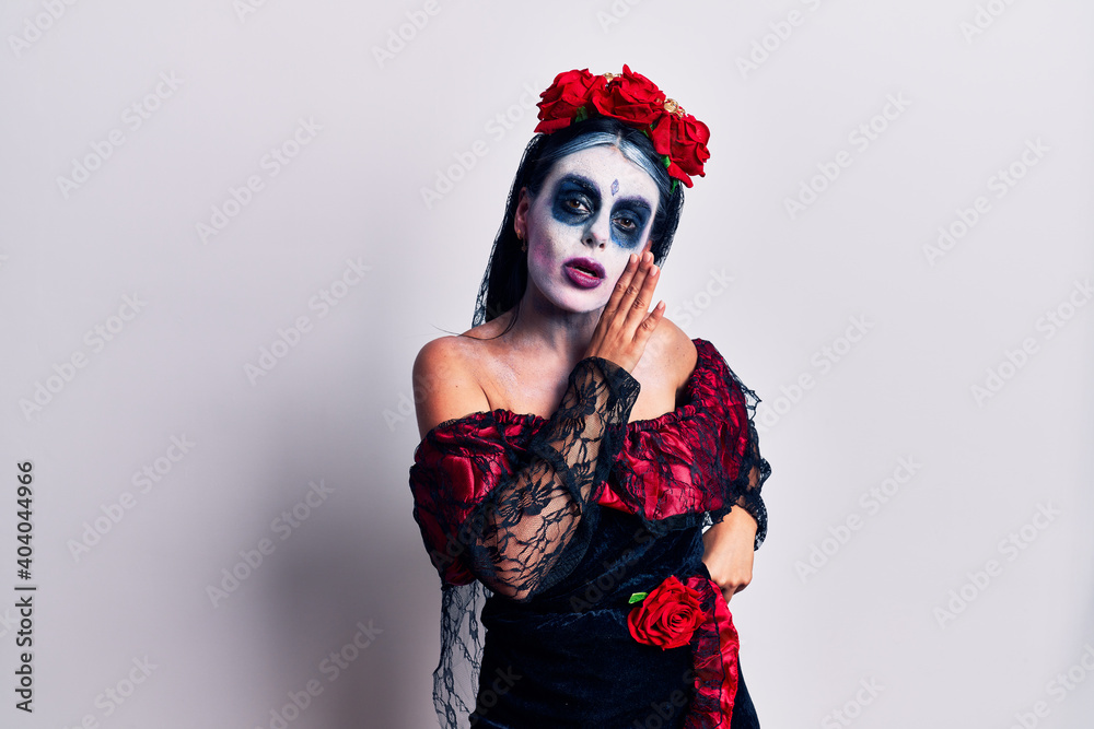 Young woman wearing mexican day of the dead makeup hand on mouth telling secret rumor, whispering malicious talk conversation