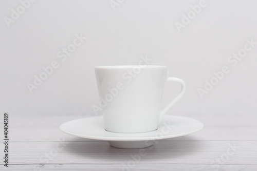 Selective focus, white ceramic tea or coffee cup with a saucer on white wooden table against white blurry background. 