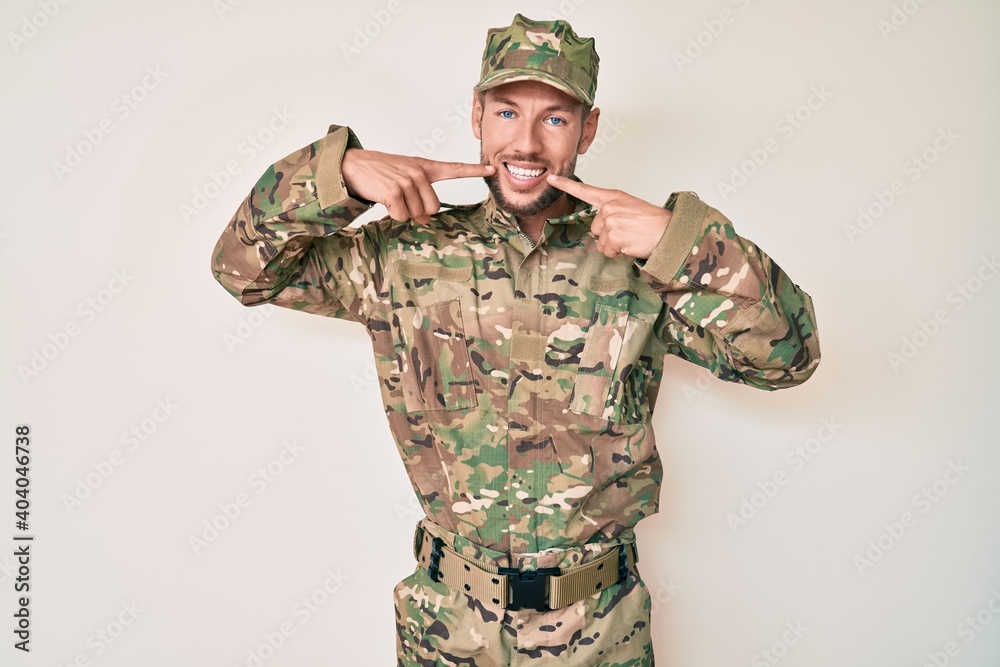 Fototapeta premium Young caucasian man wearing camouflage army uniform smiling cheerful showing and pointing with fingers teeth and mouth. dental health concept.