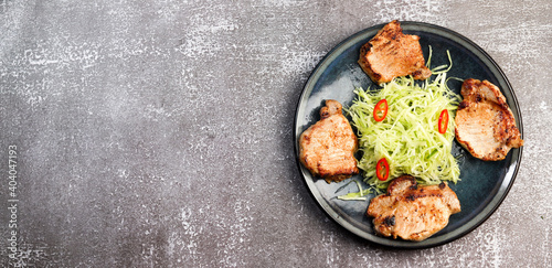 Pork loin chops with cabbage slaw on a round plate on a dark background. Top view, flat lay