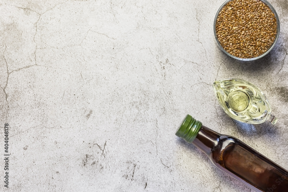 Linseed oil in a bottle, flax seeds, salad dressing in a gravy boat source of omega-3 and fatty acids on a table on a natural gray concrete background top view
