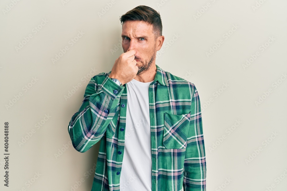 Handsome man with beard wearing casual clothes smelling something stinky and disgusting, intolerable smell, holding breath with fingers on nose. bad smell Handsome man with beard wearing casual clothes smelling something stinky and disgusting, intolerable smell, holding breath with fingers on nose. bad smell