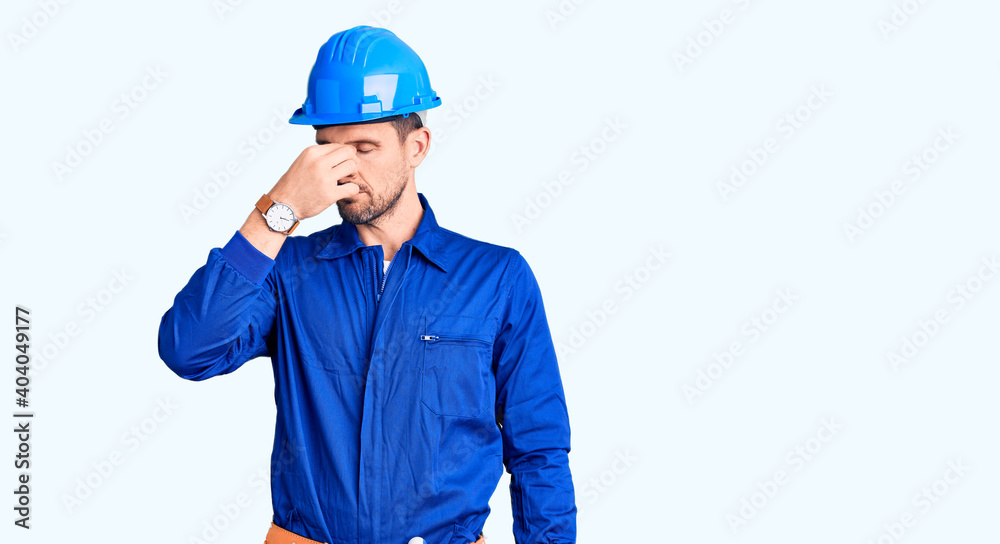 Young handsome man wearing worker uniform and hardhat strong person showing arm muscle, confident and proud of power