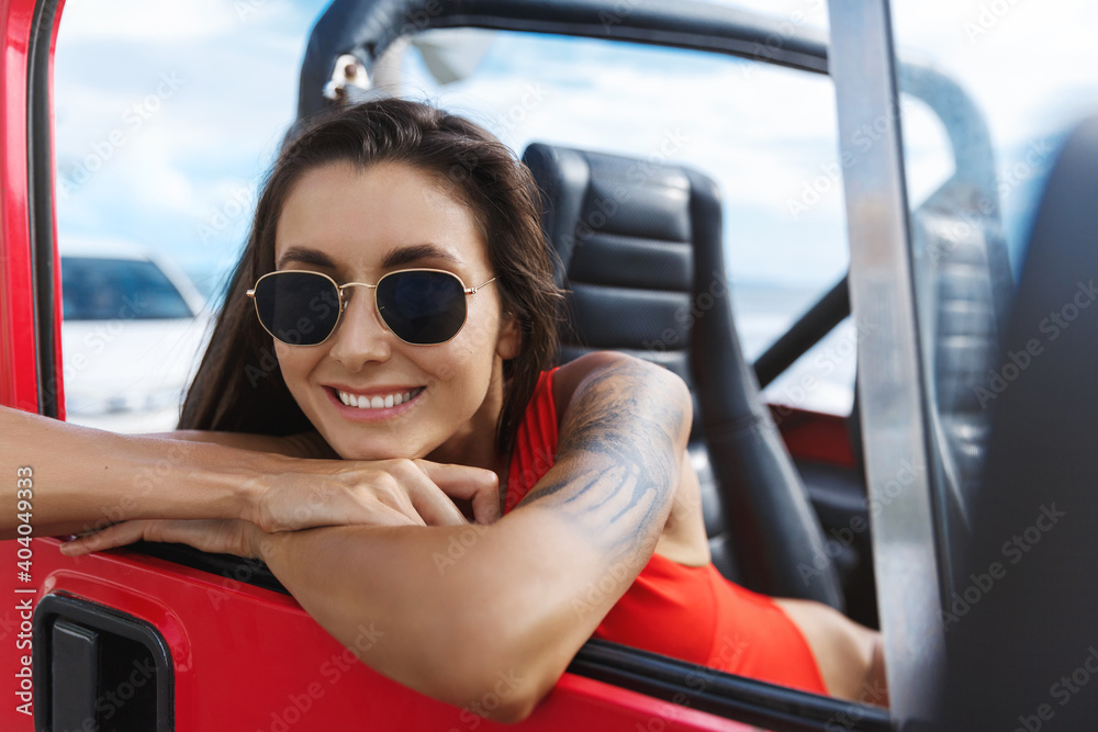 Tourism and vacation. Happy woman travel to the beach in SUV car, sitting on passanger sit in swimming suit and sunglasses. Female traveller enjoying summer holidays